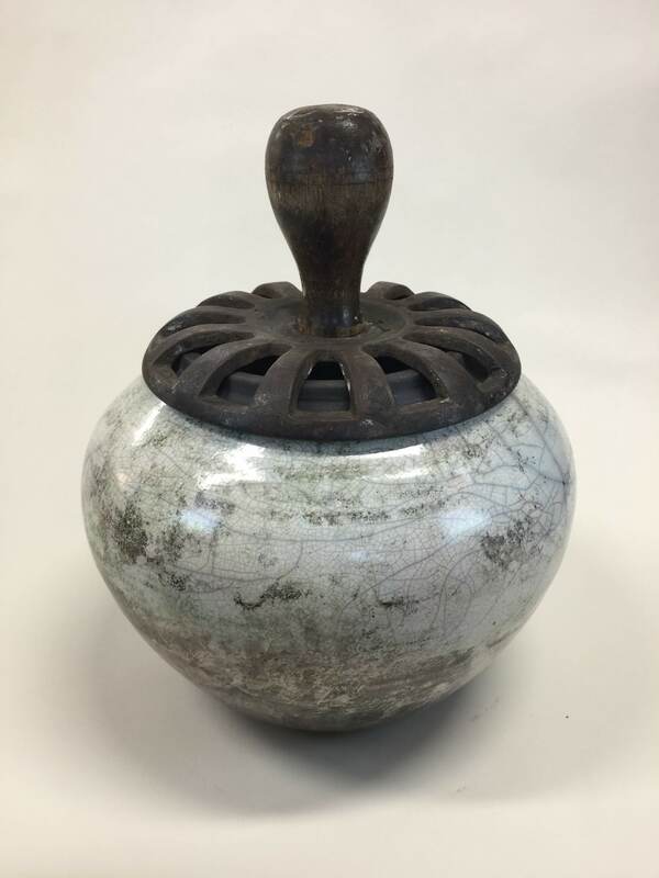 white raku fired pot with metal grate top and wooden handle